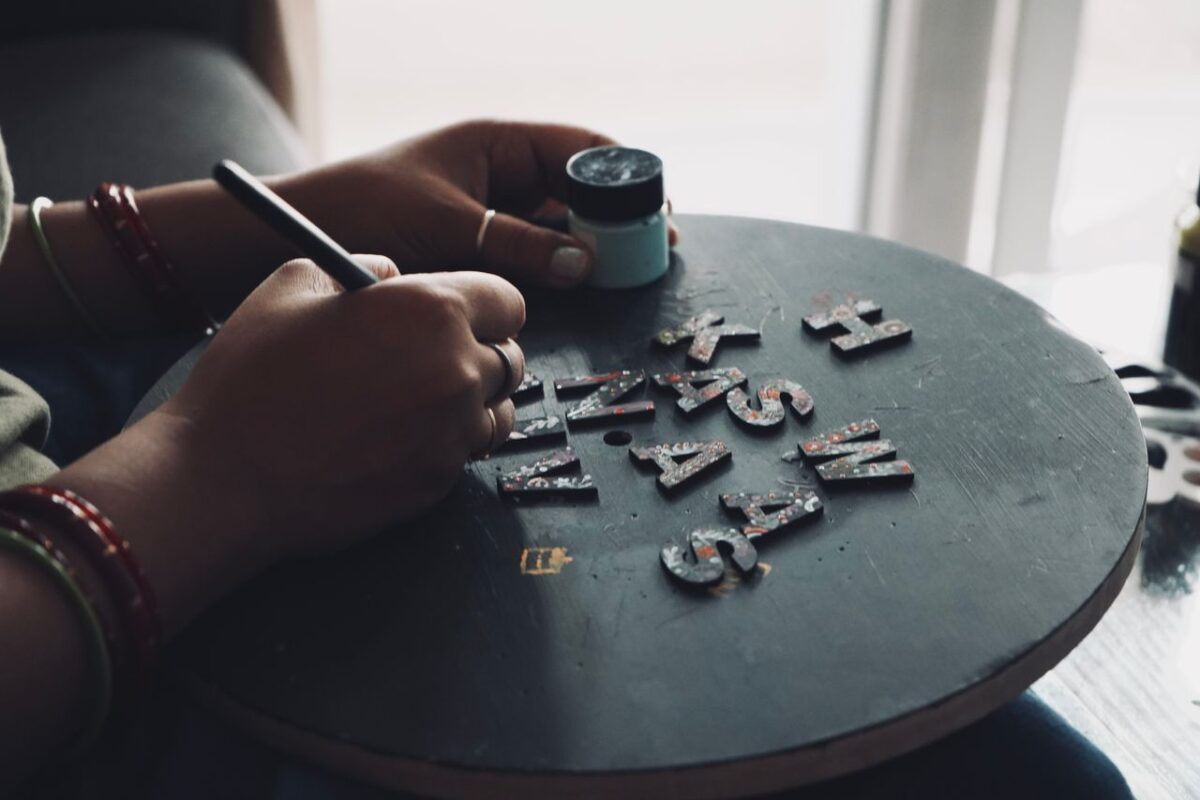 Hands painting letters on a circular board for crafting or design project.